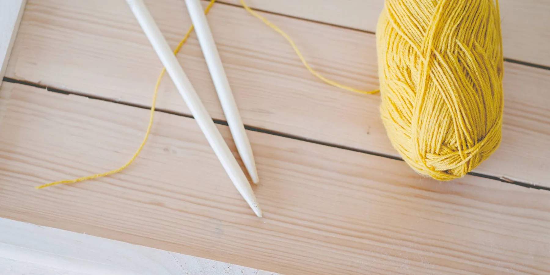 Yellow yarn with knitting needles on a wooden table